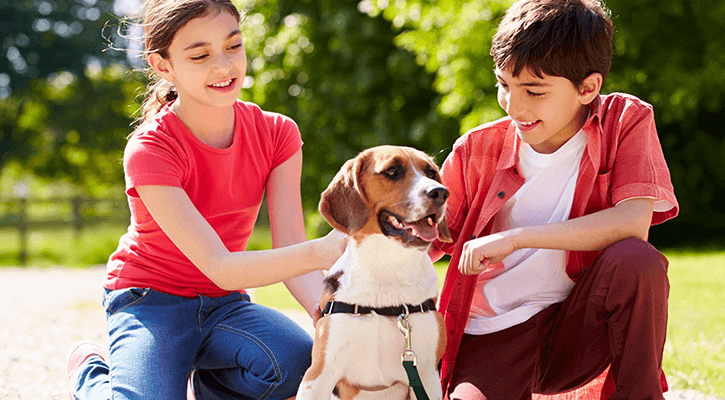 Two children sitting outside with a dog who was found using pet microchipping services